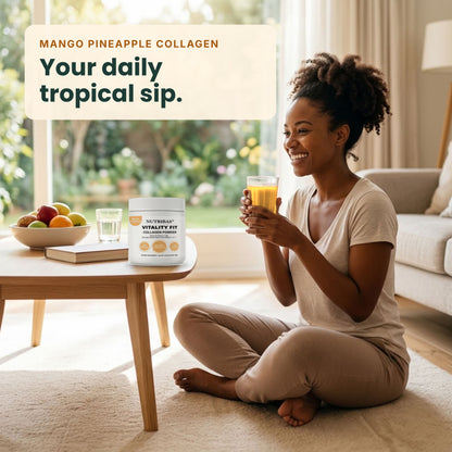 A woman sits cross-legged on a beige rug in a bright living room, holding a glass of orange drink. On the table beside her is a white tub of NutriLife365 Vitality Fizz powder labeled 'Mango Pineapple Collagen' with the text 'Your daily tropical sip.