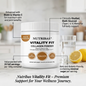A white tub of Nutribas Vitality Fit Collagen Powder is shown on a light countertop with a glass of water, lemon slices, and callout text highlighting product benefits. The product label is white with black text and brown/golden circular accents.